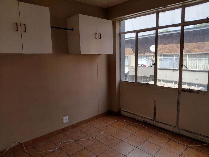 An empty bedroom featuring tiled flooring, built-in wall-mounted cabinetry, and large windows with views of the neighboring building.