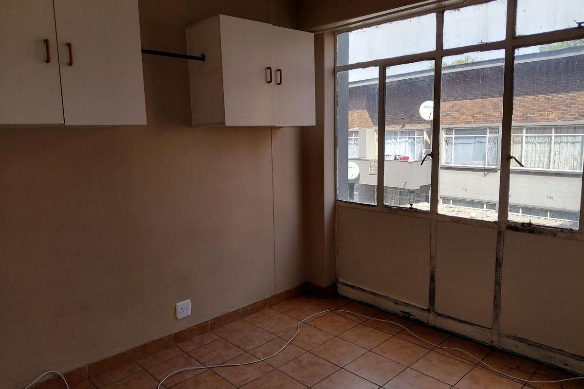 An empty bedroom featuring tiled flooring, built-in wall-mounted cabinetry, and large windows with views of the neighboring building.