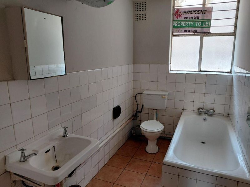 A dated bathroom featuring a bathtub, pedestal basin, and toilet with tiled walls and floors, requiring cosmetic updates and modernization.