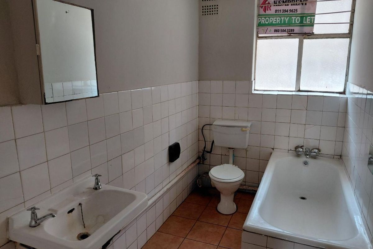 A dated bathroom featuring a bathtub, pedestal basin, and toilet with tiled walls and floors, requiring cosmetic updates and modernization.