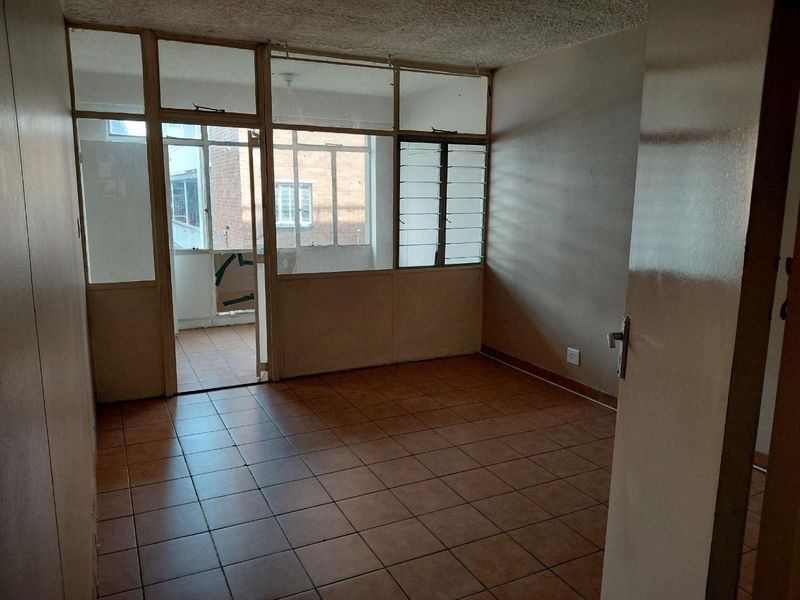 An empty living area featuring tiled flooring and a glass partition wall leading to an enclosed balcony space, requiring cosmetic updates.