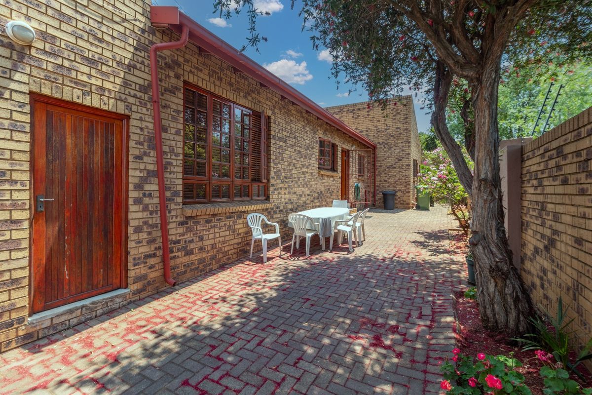 A well-maintained rear exterior view featuring a face brick facade, paved patio area, and established garden surroundings.