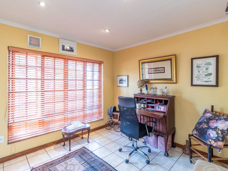 A functional home office space featuring tiled flooring, recessed downlighting, and large windows fitted with wooden venetian blinds.