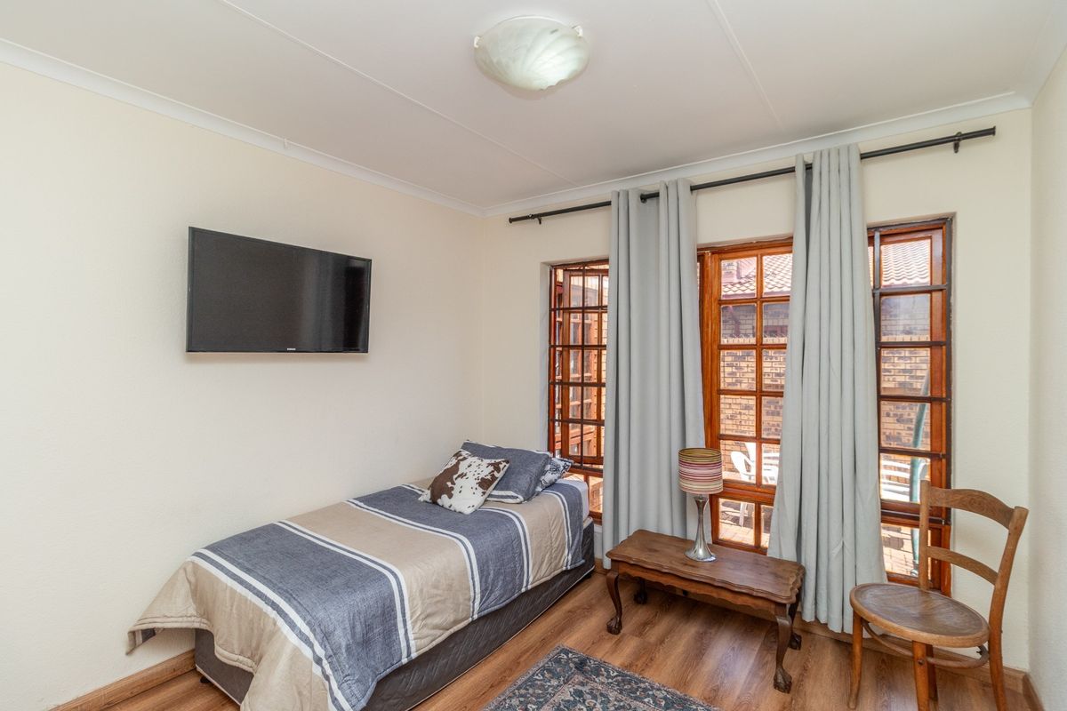 A functional bedroom featuring laminate flooring, wooden framed windows, and neutral wall finishes, providing a comfortable and well-lit living space.