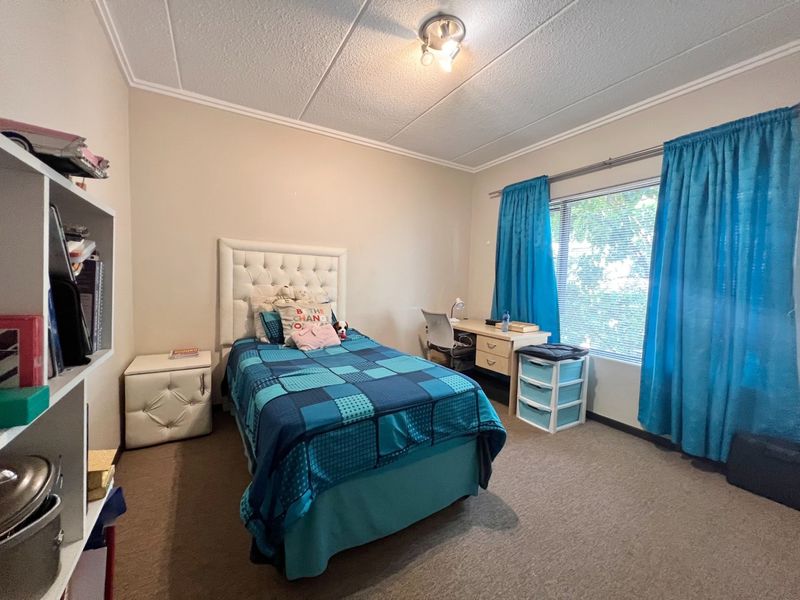 A functional bedroom featuring neutral walls, carpeted flooring, and a large window with curtain rod, providing ample natural light.