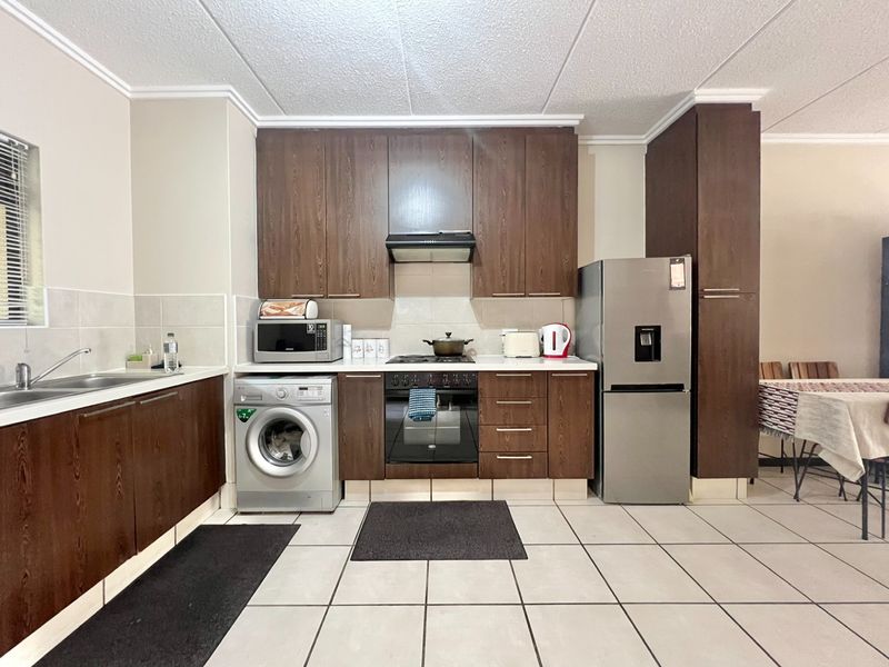 A functional kitchen featuring dark wood-look cabinetry, built-in oven with extractor fan, tiled flooring, and a double sink with tiled backsplash.