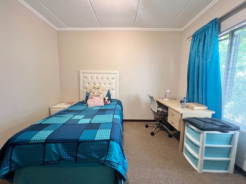 A functional bedroom featuring carpeted flooring, acoustic ceiling tiles, and a window with fitted blinds, providing a comfortable and practical living space.