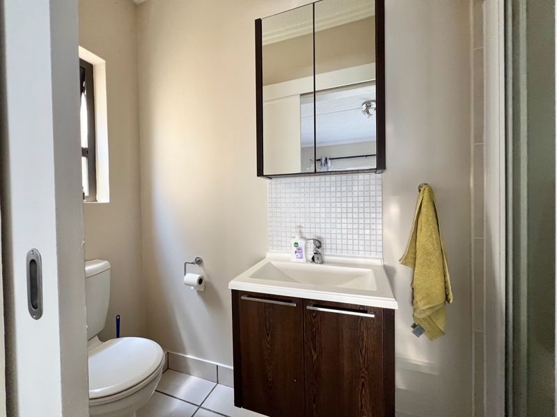 A functional bathroom featuring a vanity cabinet with a basin, mirrored medicine cabinet, tiled splashback, toilet, and a shower enclosure.