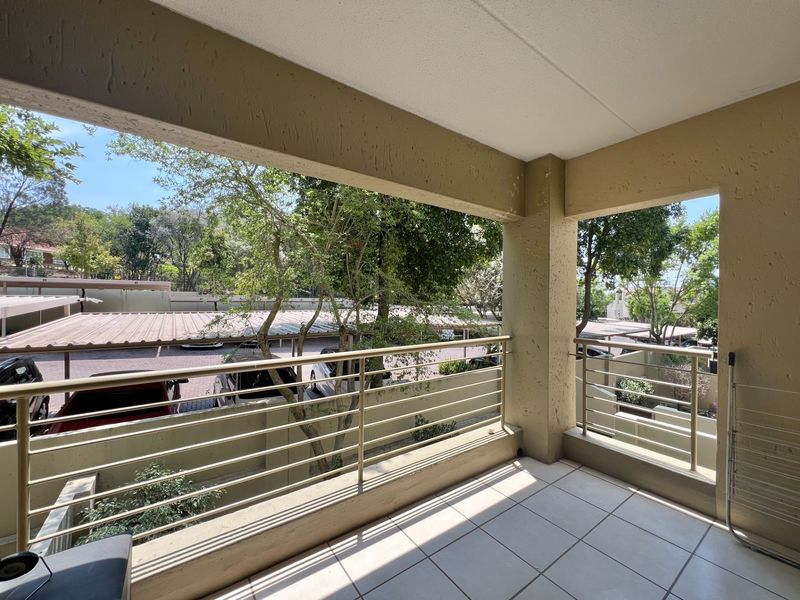 A covered balcony featuring tiled flooring and a metal balustrade, offering an outdoor space with views of the complex parking area.