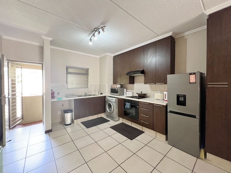 A functional kitchen featuring dark wood cabinetry, built-in oven with hob, extractor fan, double sink, and tiled flooring, with direct access to an outdoor area.