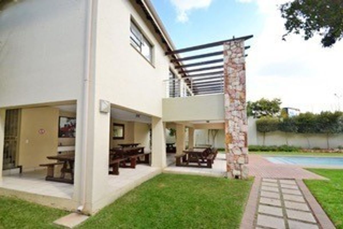 Rear view of the property featuring a spacious covered patio with a stone-clad pillar, overlooking a well-maintained garden and swimming pool area.