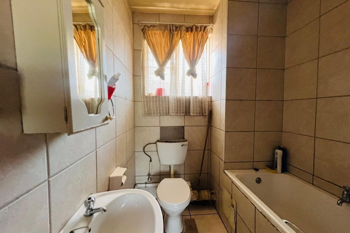 A compact bathroom featuring a bathtub, pedestal basin, and toilet with tiled walls and flooring, offering potential for modernization.