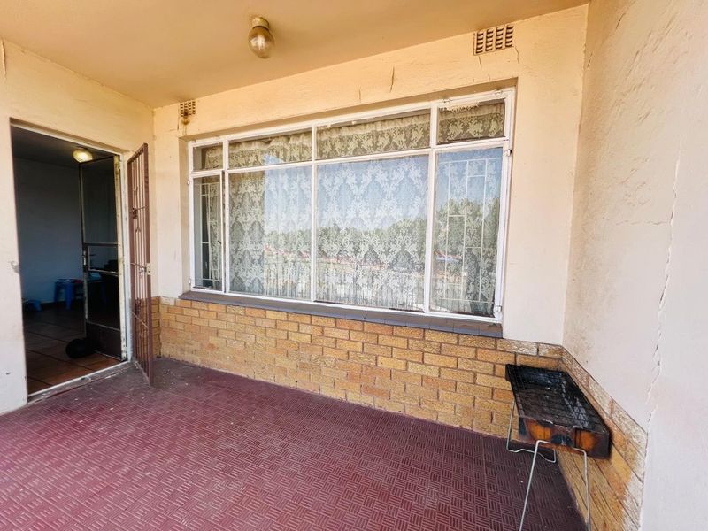A covered patio area featuring brick wall detailing, tiled flooring, and a large window, offering a functional outdoor space in need of cosmetic updates.