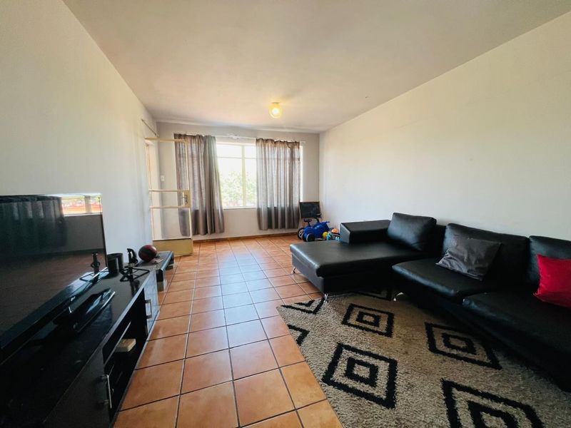 A spacious living room featuring tiled flooring, neutral walls, and natural light from a large window and glass panel door.