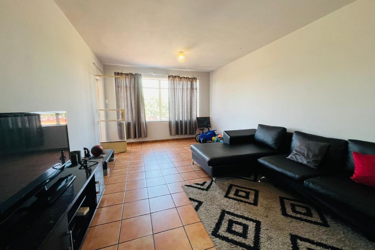 A spacious living room featuring tiled flooring, neutral walls, and natural light from a large window and glass panel door.