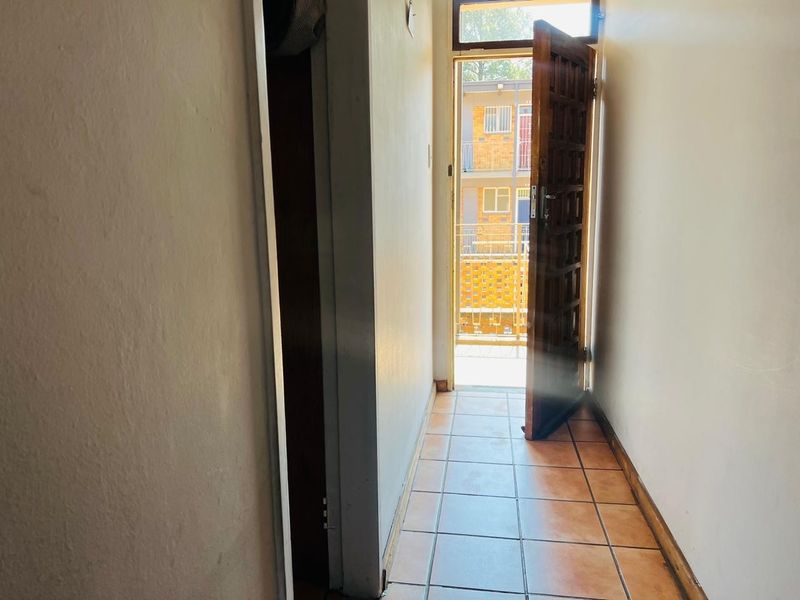 A simple entrance hallway featuring tiled flooring and a wooden door leading to an exterior balcony area.