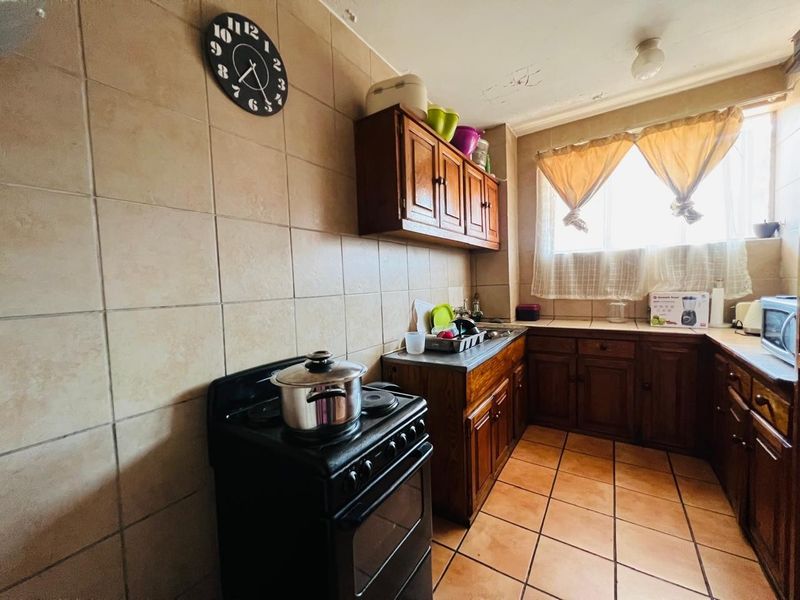 A dated kitchen featuring wooden cabinetry, tiled walls and flooring, and a freestanding stove, requiring cosmetic updates to the ceiling and finishes.