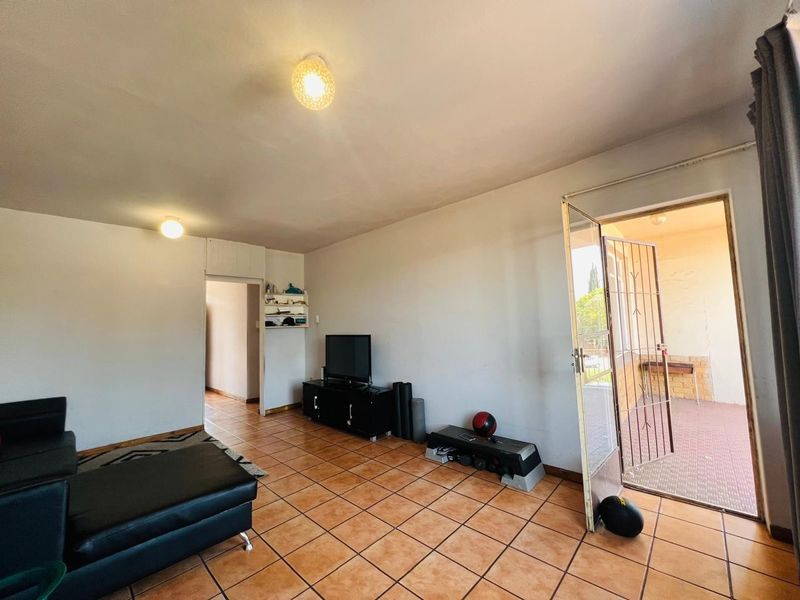 A living room featuring tiled flooring, built-in shelving, and direct access to an outdoor patio area through a security gate.