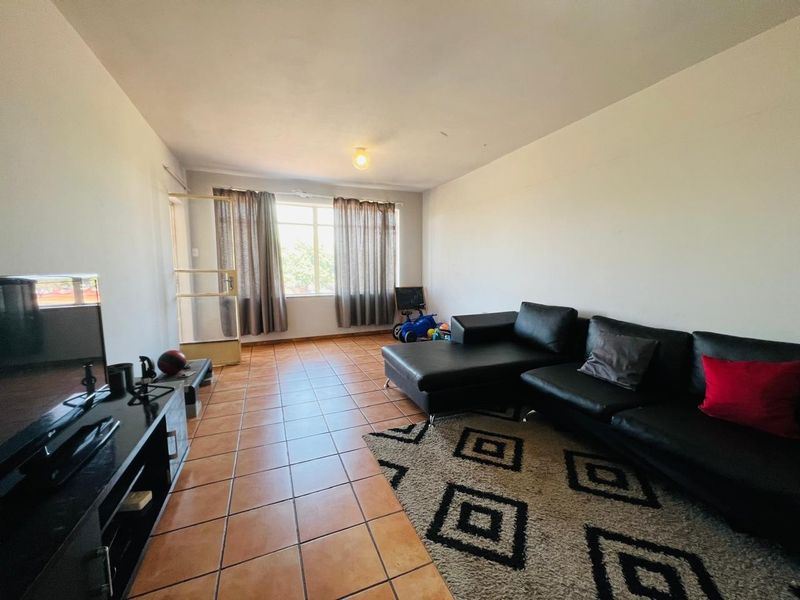 A spacious living room featuring tiled flooring, neutral walls, and a large window allowing for natural light.