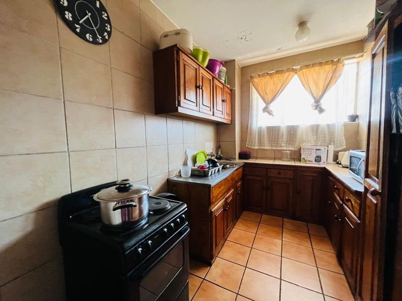 A compact kitchen featuring wooden cabinetry, tiled walls and flooring, and a freestanding stove, requiring cosmetic updates to the ceiling and finishes.