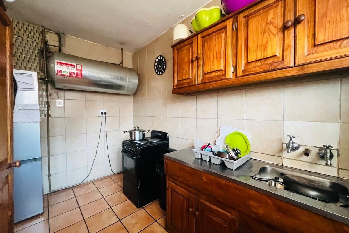 A functional kitchen featuring wooden cabinetry, a stainless steel sink, tiled backsplash, and a wall-mounted electric water heater.