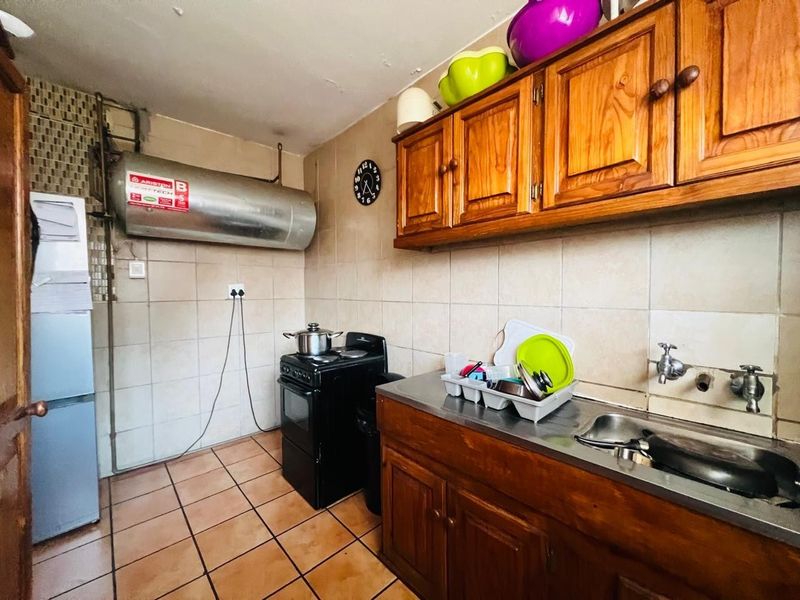 A functional kitchen featuring wooden cabinetry, a stainless steel sink, tiled backsplash, and a wall-mounted electric water heater.