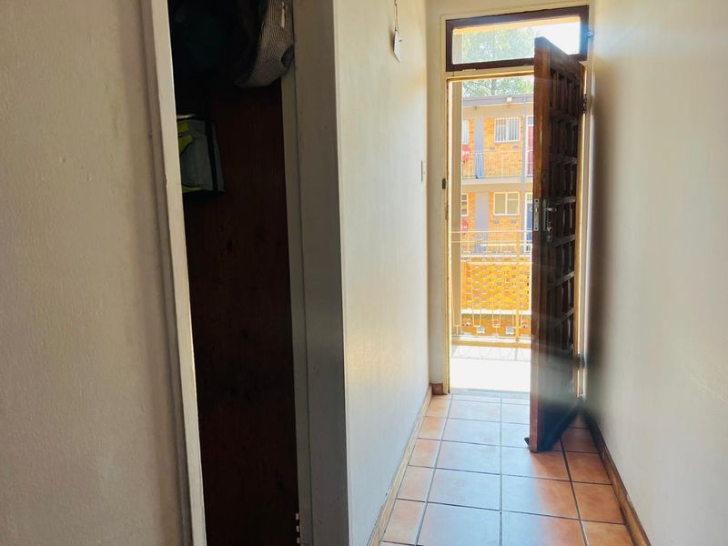 An entry hallway featuring tiled flooring, a built-in cupboard, and a wooden entrance door leading to an exterior balcony.