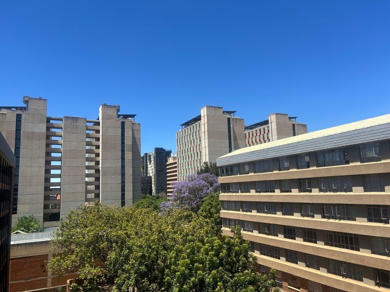 An elevated urban view showcasing surrounding multi-story apartment buildings and mature greenery under a clear blue sky.
