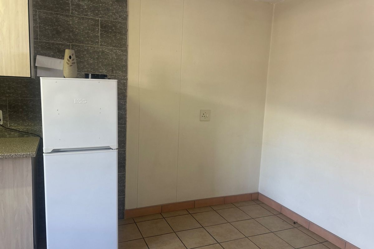A functional kitchen area featuring tiled flooring, a tiled splashback, and built-in cabinetry with countertop space.