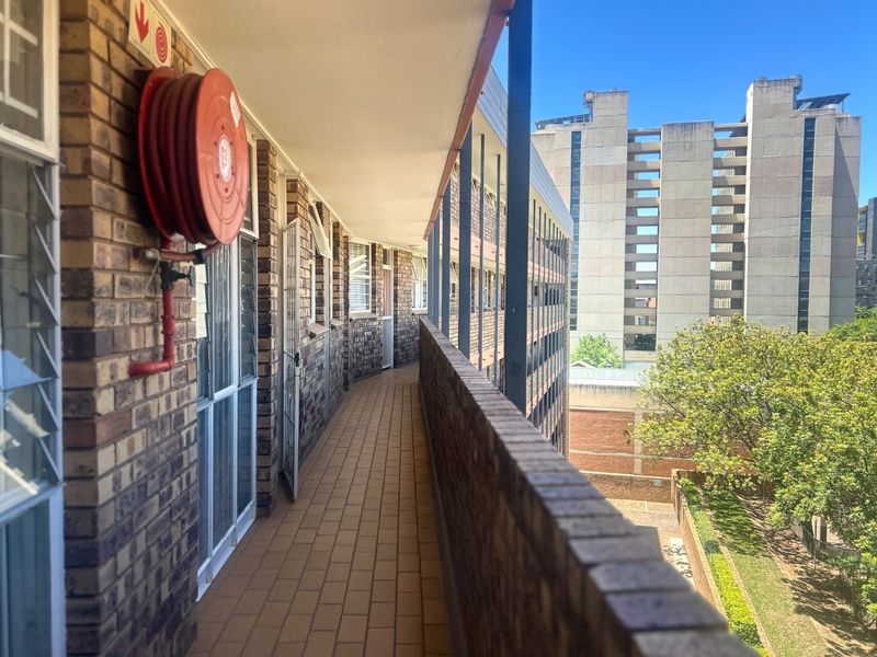 An exterior apartment balcony featuring brick masonry, tiled flooring, and a mounted fire hose reel, overlooking the surrounding building complex.