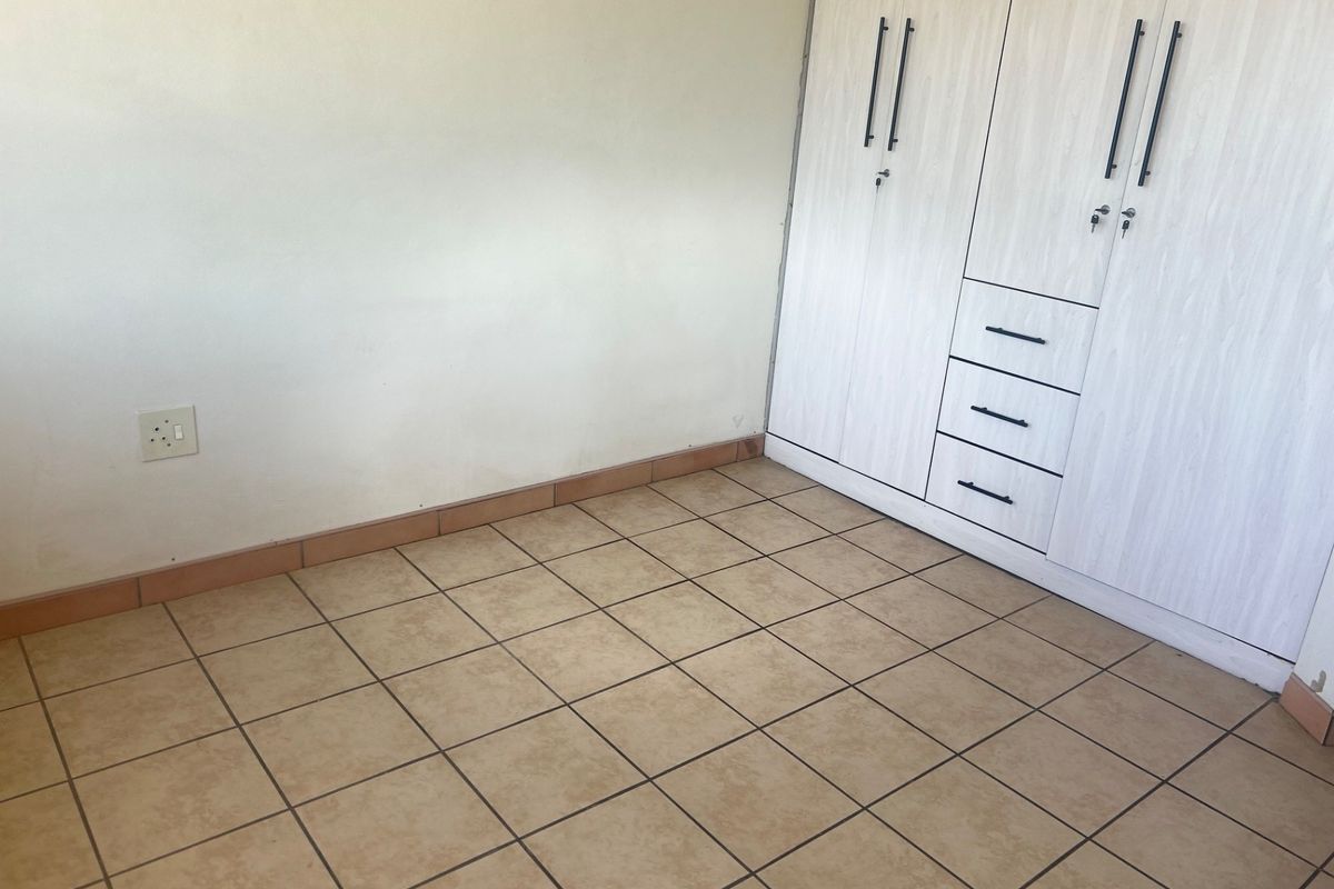 A clean, empty bedroom featuring neutral tiled flooring and built-in wooden cupboards with integrated drawers.