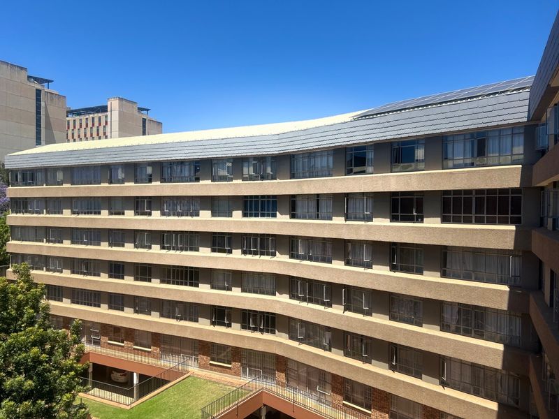 A multi-story apartment building exterior featuring a curved facade, concrete balconies, and a tiled roof with integrated solar panels.