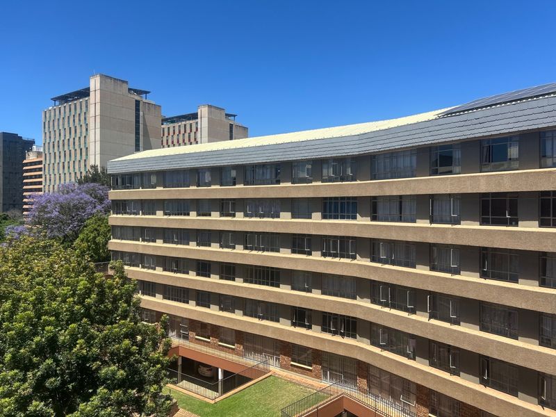 An exterior view of a multi-story apartment building featuring a curved facade, tiled roofing, and metal-framed windows set within an urban environment.
