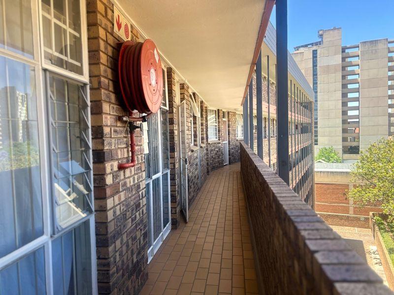 An exterior balcony walkway featuring brick walls, tiled flooring, and a mounted fire hose reel in an apartment complex setting.