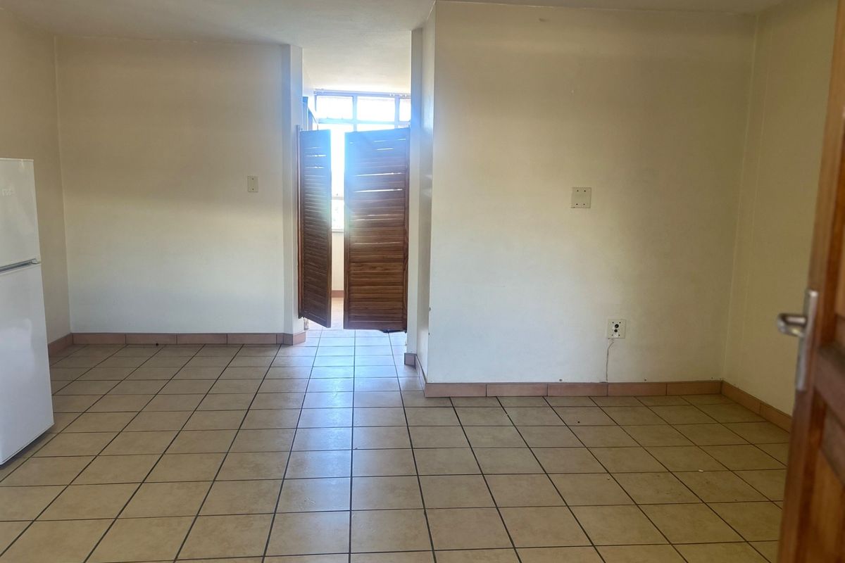 An empty living area featuring ceramic tile flooring and wooden louvered doors leading to an adjacent space, offering a blank canvas for interior design.