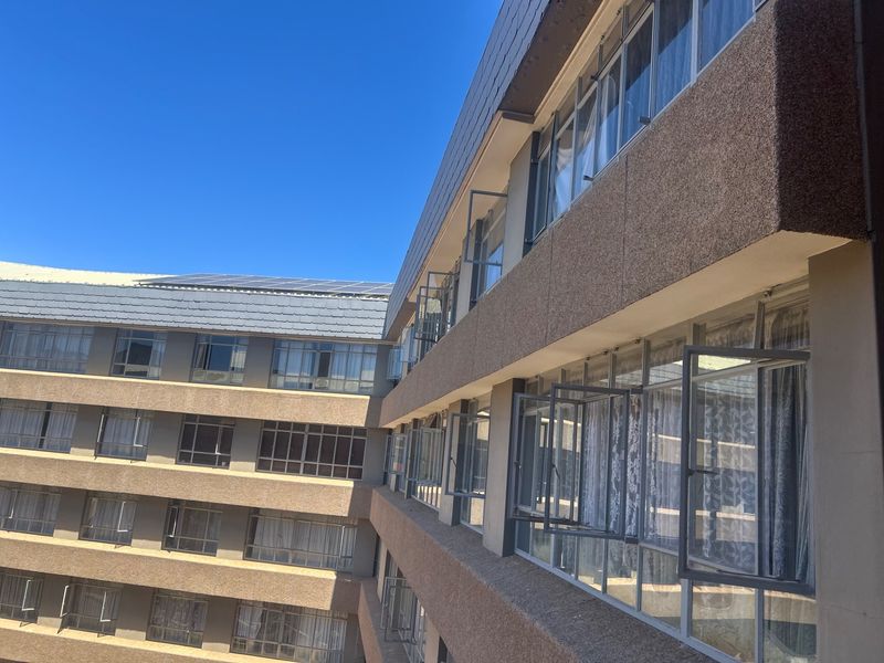 Exterior view of an apartment building facade featuring multiple levels of casement windows and a tiled roof with solar panel installation.