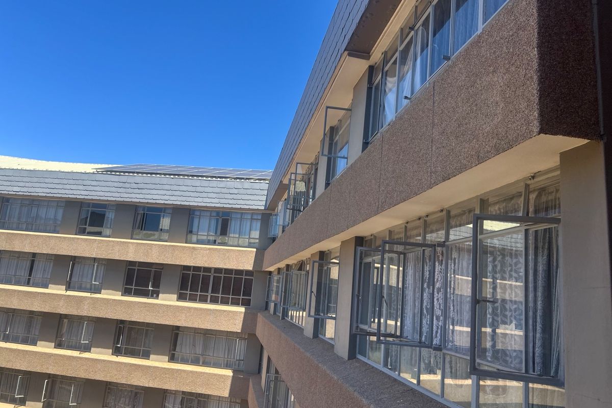 Exterior view of an apartment building facade featuring multiple levels of casement windows and a tiled roof with solar panel installation.