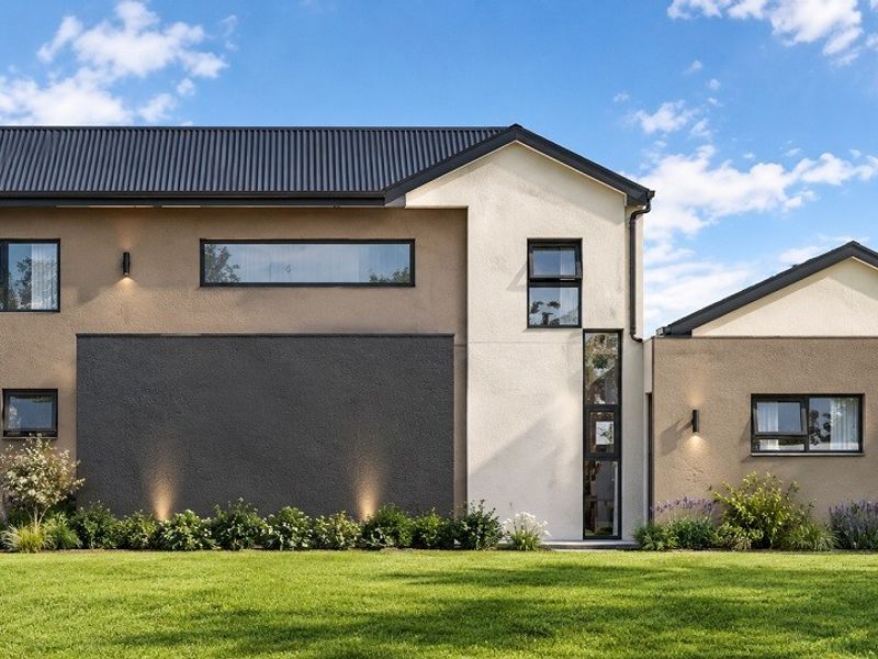 Modern two-story residential exterior featuring a combination of textured render finishes, dark metal roofing, and large aluminum-framed windows overlooking a manicured lawn.