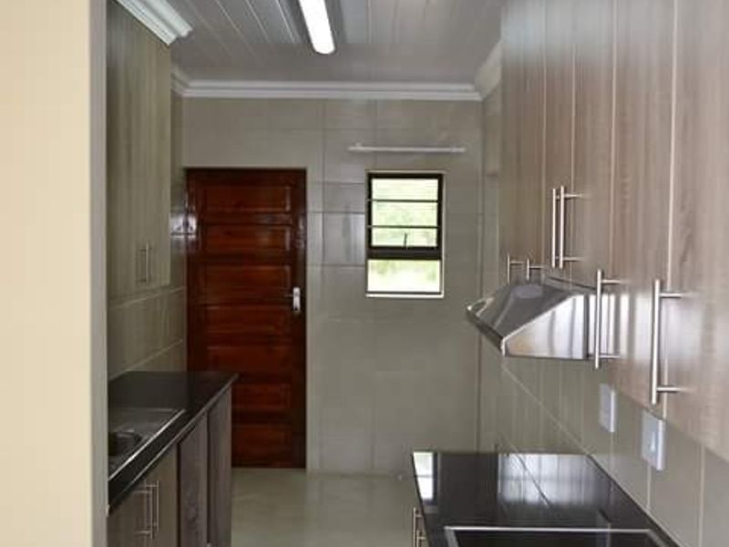 A clean, modern kitchen featuring granite countertops, built-in cabinetry, a stainless steel extractor fan, and tiled flooring with a neutral color palette.