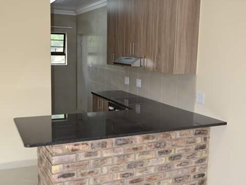 Modern kitchen featuring a unique exposed brick breakfast bar, granite countertops, ample built-in cabinetry, and a clean, tiled finish throughout.