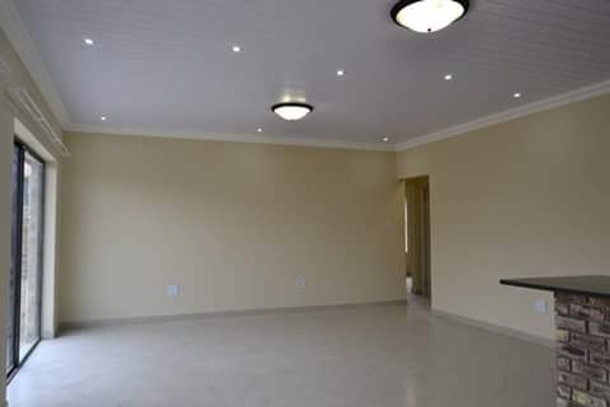 Spacious, empty living area featuring tiled floors, a tongue and groove ceiling with recessed lighting, and a brick-based breakfast bar.