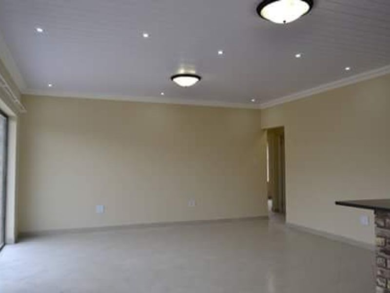 Spacious, empty living area featuring tiled floors, a tongue and groove ceiling with recessed lighting, and a brick-based breakfast bar.