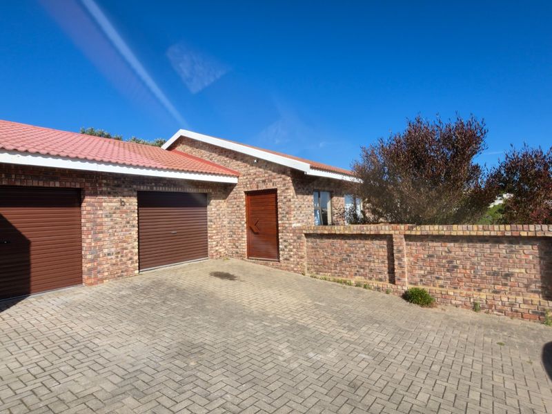 Front exterior view of a face brick house featuring a double garage, paved driveway, and secure boundary walling under a clear sky.