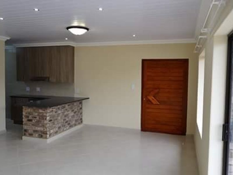 Open plan living area featuring a modern kitchen with stone-clad breakfast bar, tiled flooring, recessed lighting, and direct access to an outdoor space.