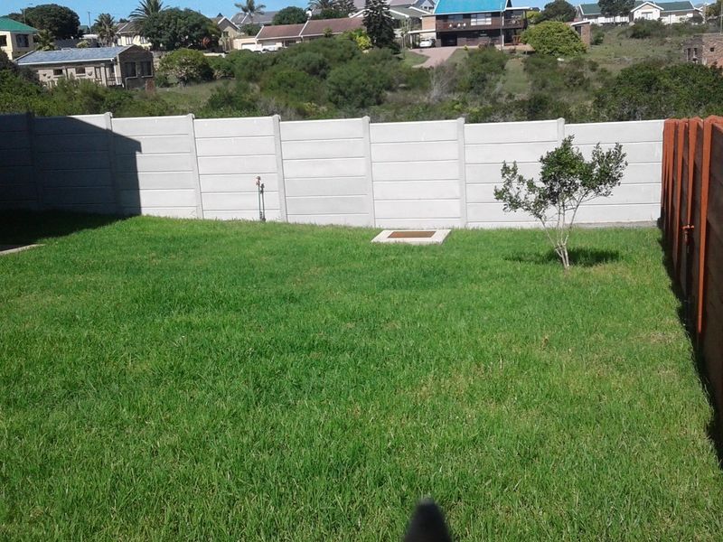 A private rear garden featuring a well-maintained lawn, enclosed by a combination of precast concrete boundary walls and timber fencing.