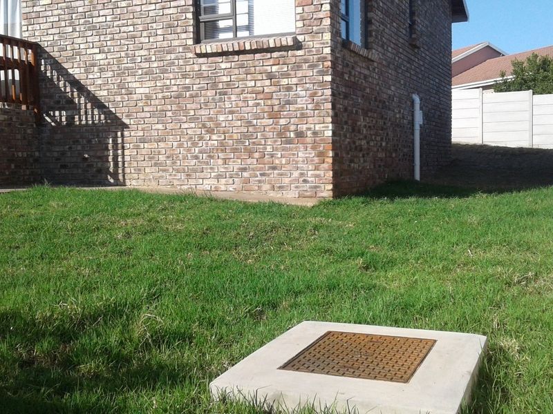 Rear exterior view of the property featuring a brick facade, a raised wooden deck, and a private garden area with a concrete inspection cover.