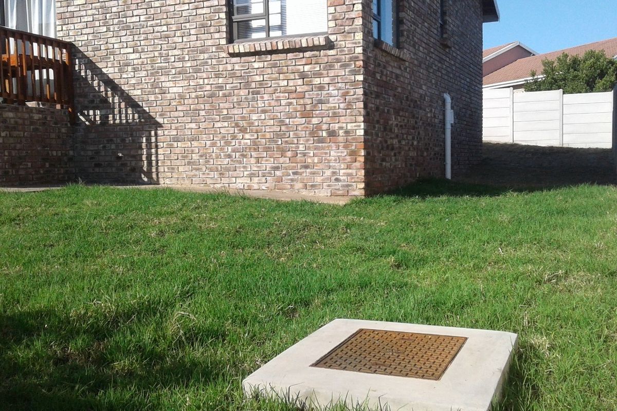 Rear exterior view of the property featuring a brick facade, a raised wooden deck, and a private garden area with a concrete inspection cover.