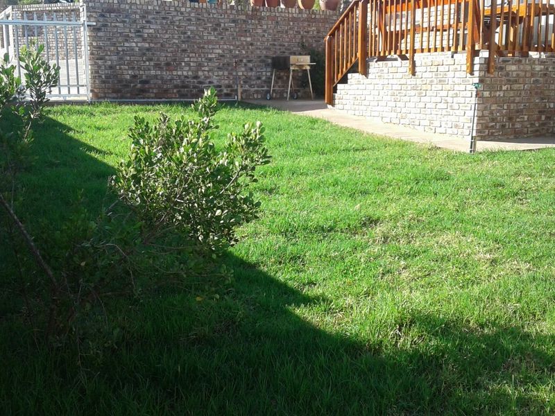 A well-maintained garden area featuring a lush lawn, face brick boundary walls, and an elevated timber deck with a wooden balustrade.