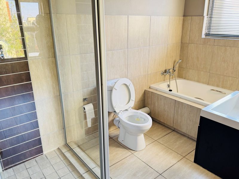 A clean, modern bathroom featuring a built-in bathtub, a separate glass-enclosed shower, and neutral wall and floor tiling.
