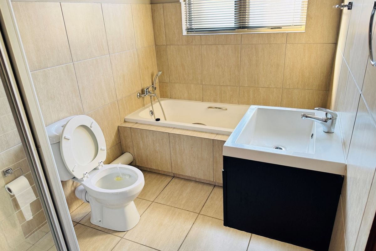 A functional bathroom featuring a built-in bathtub, vanity basin, and wall-mounted toilet with neutral floor-to-ceiling tiling.